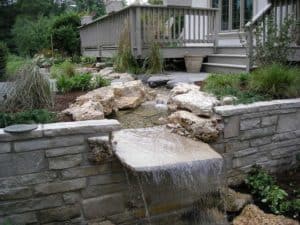 A stone slab, extending beyond a Lannon stone wall, creates a simple, naturalistic waterfall in this Long Grove, Illinois garden.