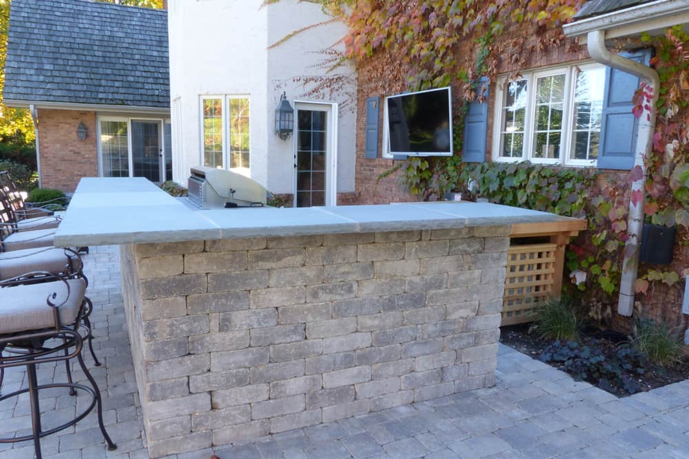 lake-forest-after An outdoor bar becomes the center of activity. Made of the same tumbled concrete used for the new patio, and featuring a bluestone top, the bar integrates a built-in grill as well as preparation and serving areas.