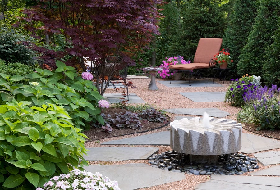 granite-millstone-fountain Off of the patio, a path of crushed red granite and broken flagstone meander toward another, more private seating area. Midway down the path you’ll find a gently bubbling granite millstone fountain surrounded by smooth river rock—the sound of the water attracting birds to this area of the garden. Along the edges of the path are a variety of bushes, flowers and trees, including a magnificent purple Japanese maple—each chosen by the homeowner and Van Zelst’s landscape designers specifically for their texture, height, color and ability to thrive in the area.