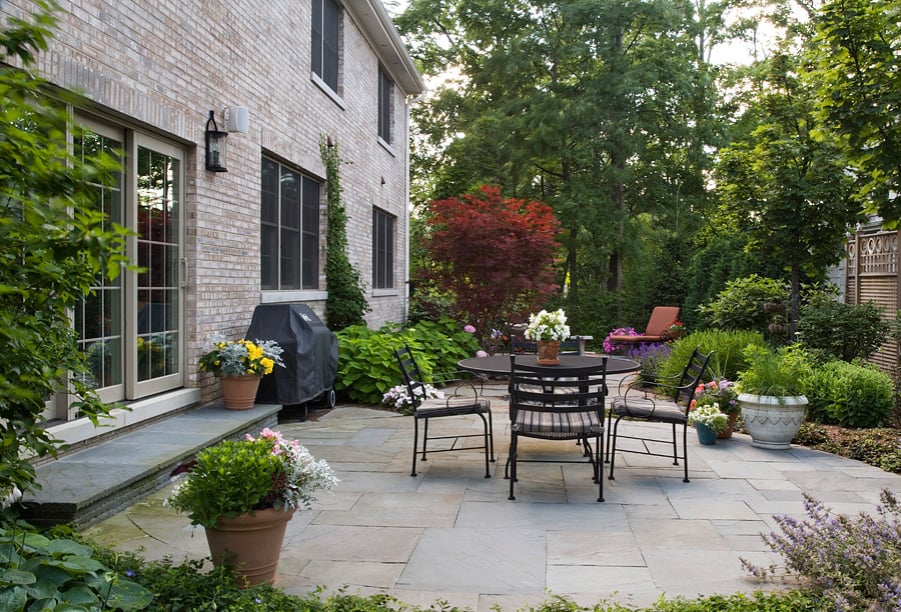 highland-park-il-bluestone-patio The generous patio area features beautiful yet practical bluestone pavers as its foundation; a rugged, slip-proof material, bluestone will weather the Chicago-area’s cold winters and warm summers. The classically-styled dining table and chairs create a great area for a meal or a conversation, and thoughtfully placed container and in-ground plants add lush greenery and welcome pops of color to the area.